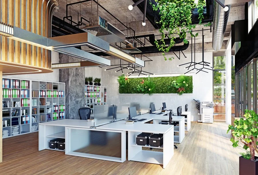Modern office space with white desks, black chairs, floor-to-ceiling windows, and vibrant green plants.