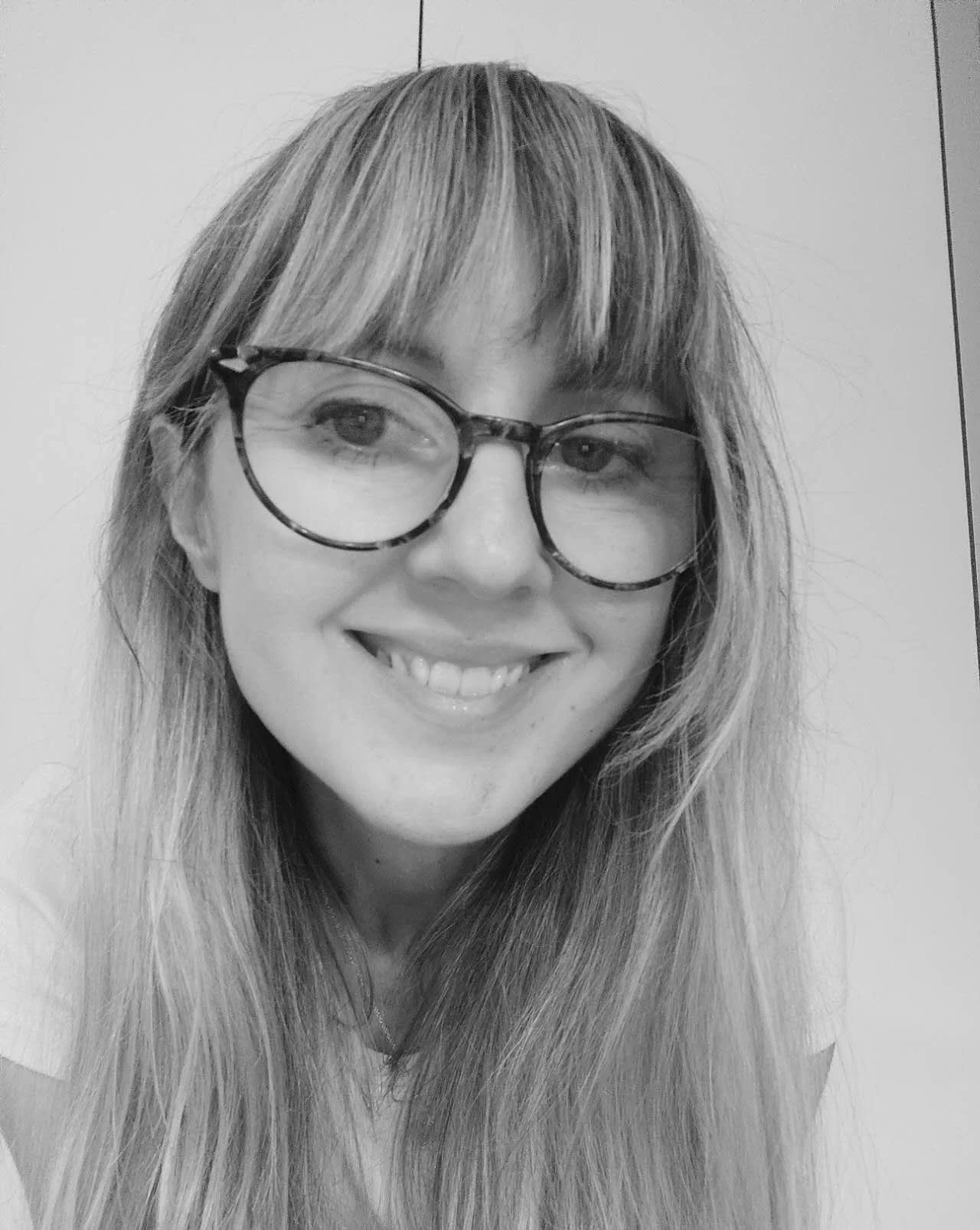 Black and white photo of a smiling woman wearing glasses with long hair and bangs.